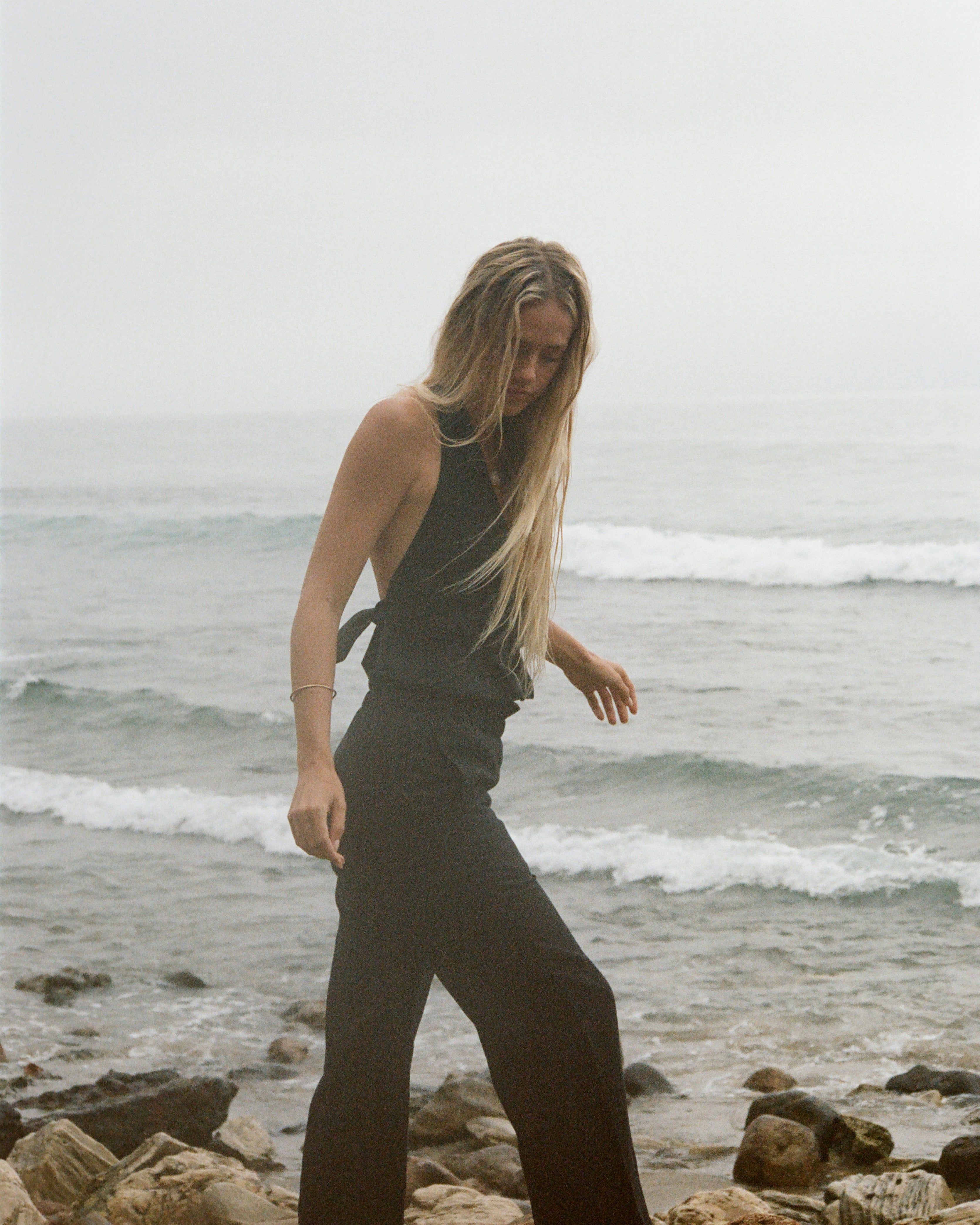 Woman in black set walking along a rocky beach with ocean waves in the background