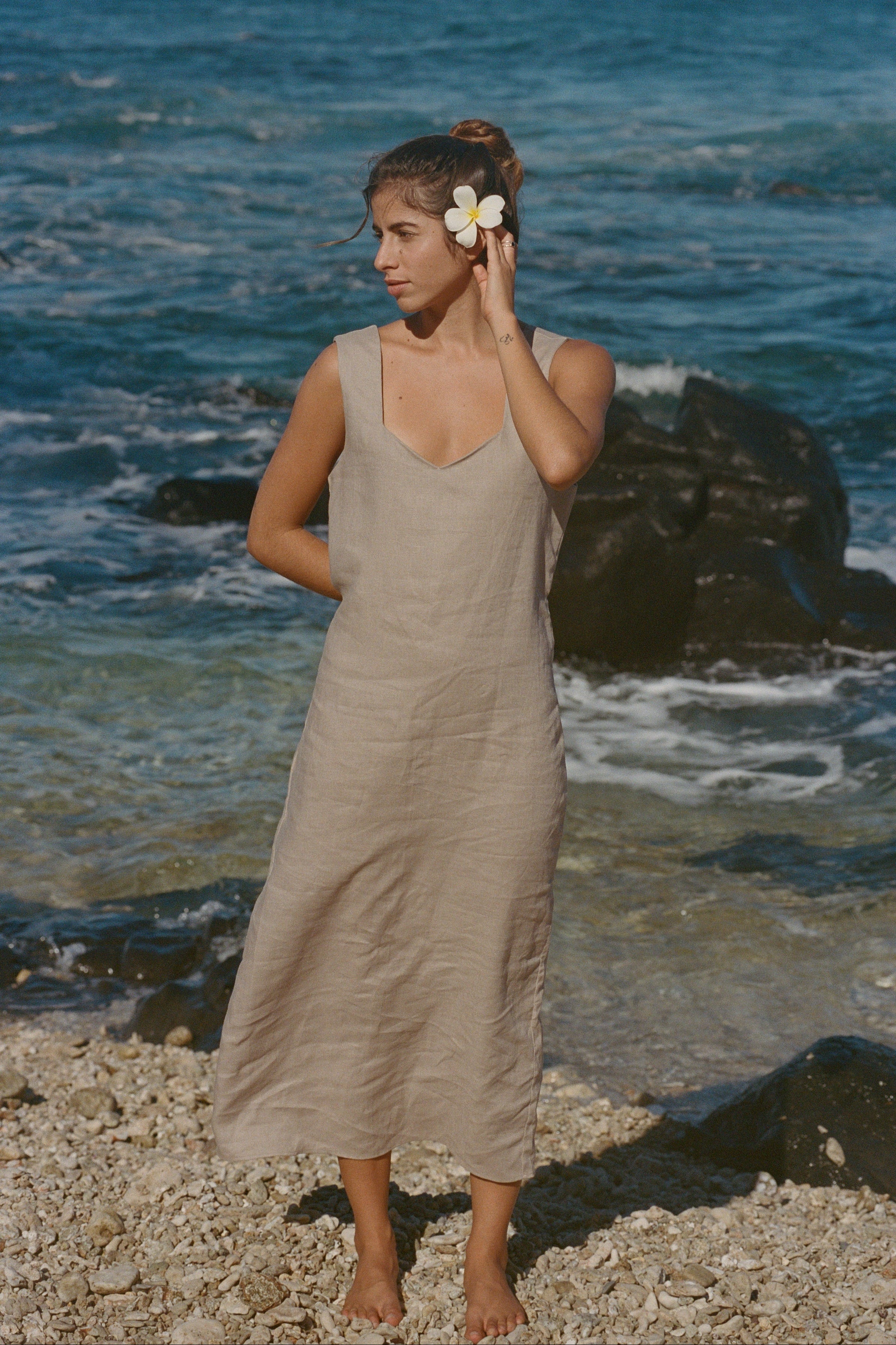 Woman in a beige dress standing on a beach with ocean waves in the background