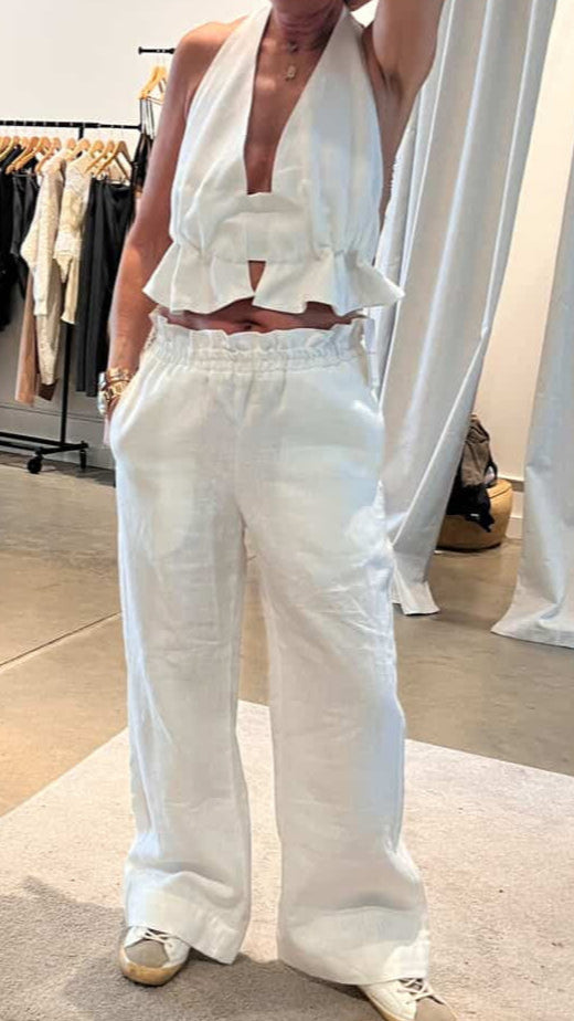 Person wearing a white outfit with ruffled top and wide-leg pants in a clothing store.