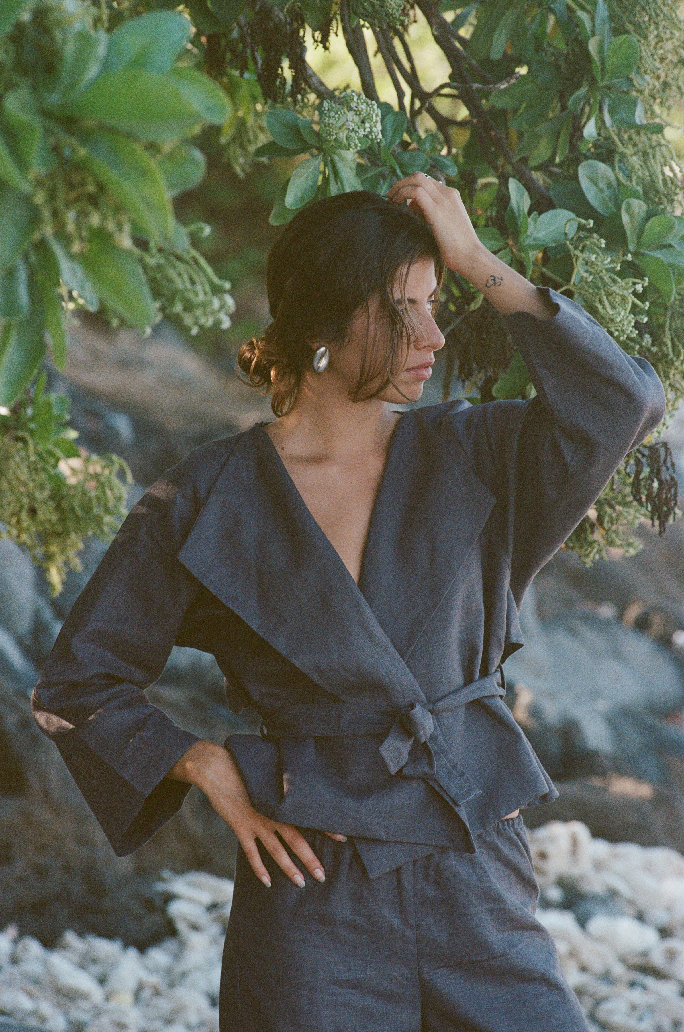 Woman in a charcoal linen outfit standing among green foliage