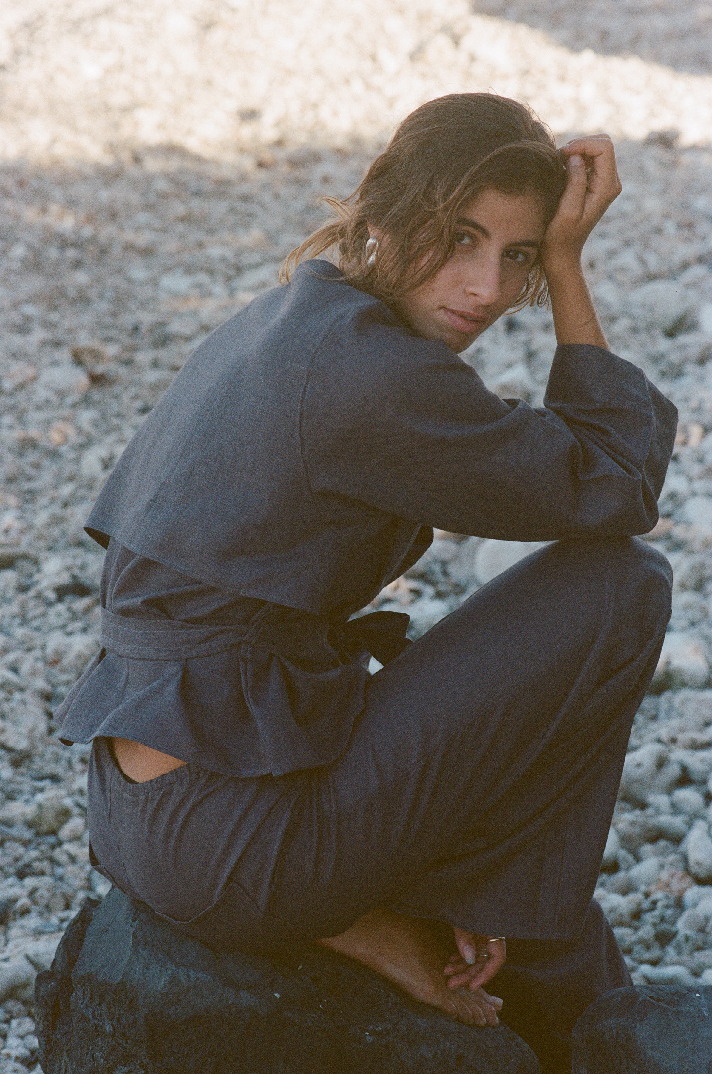 Model wearing a charcoal linen set sitting on a rocky surface