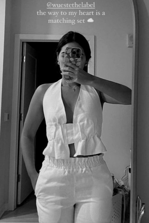 Person taking a mirror selfie wearing a white outfit with text on the wall.